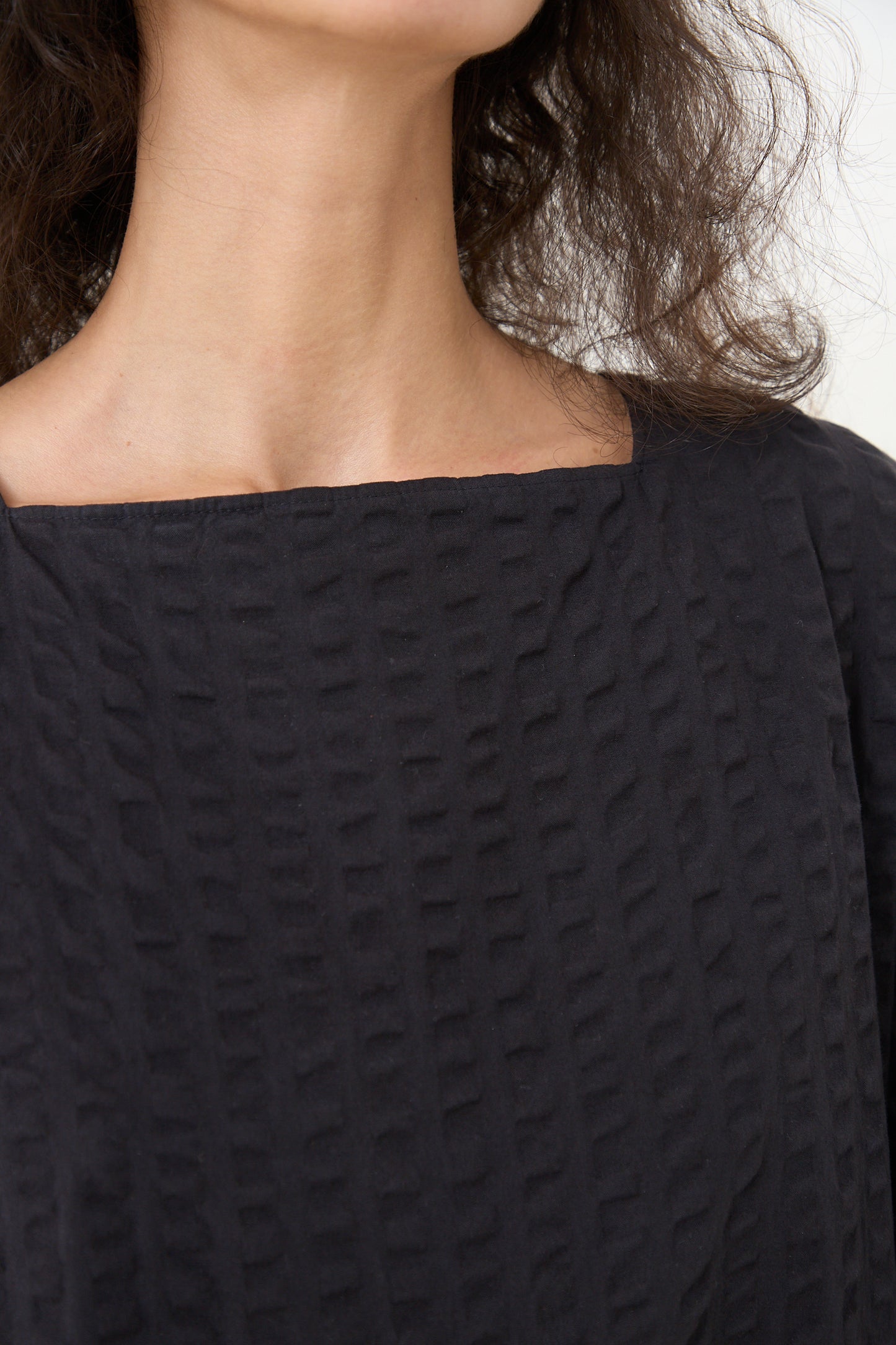A close-up image showing the lower face and neckline of a person wearing a Cotton Seersucker Tradi Dress in Ink Black designed by Black Crane, Los Angeles.