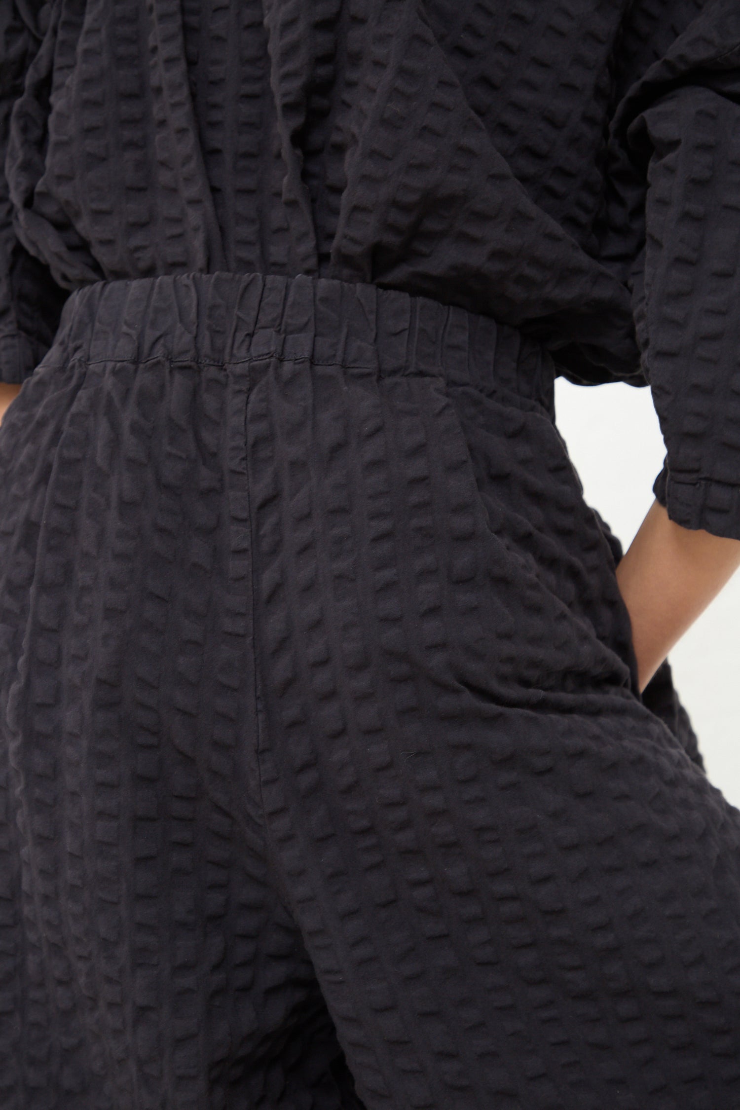 A close-up of a person wearing a Cotton Seersucker Wide Pant in Ink Black from Black Crane with an elastic waistband.