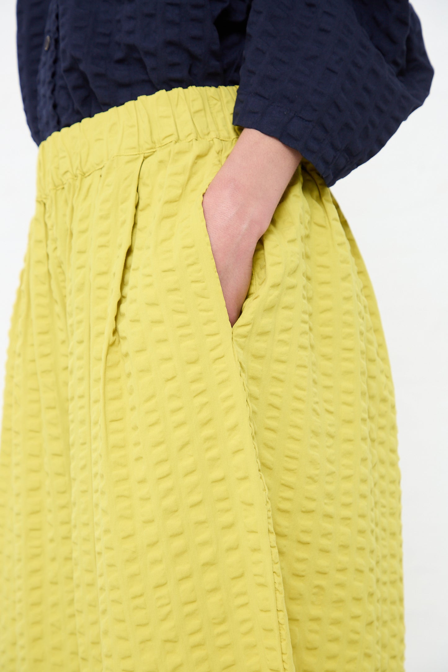 A person standing with their hand in the pocket of a yellow textured, Black Crane Cotton Seersucker Wide Pant in Turmeric.