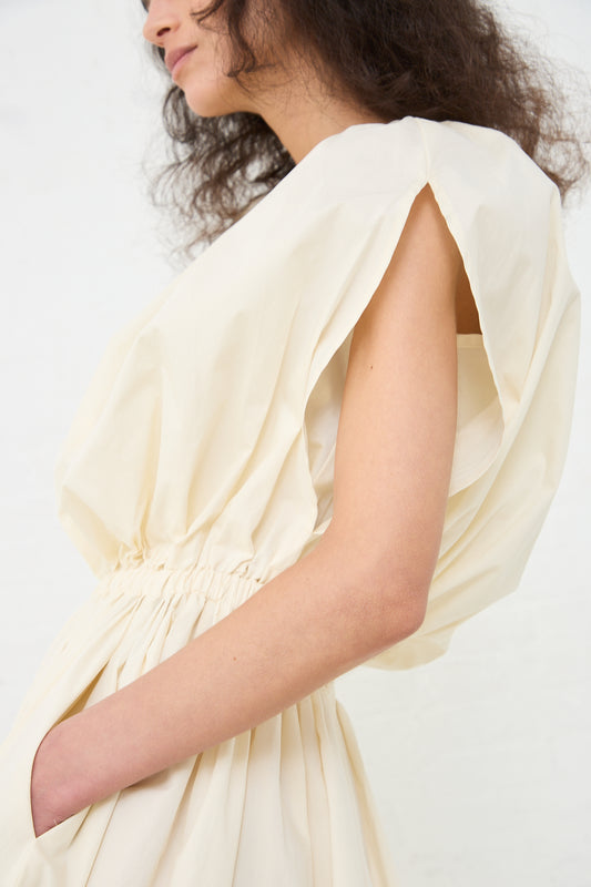 Profile view of a person wearing an elegant Black Crane Organic Cotton Shell Dress in Cream with draped sleeves.