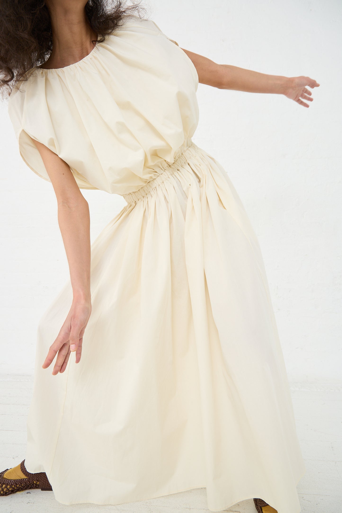 Woman in a Black Crane Organic Cotton Shell Dress in Cream, with gathered waist detailing, posing against a white background.