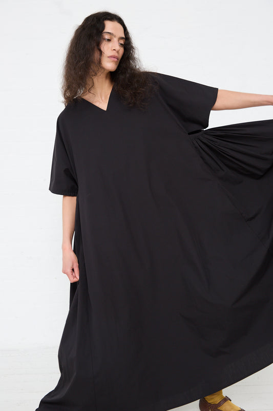 Woman in a flowing Black Crane Organic Cotton Star Neck Dress in Black, posing with one hand holding the garment's fabric.