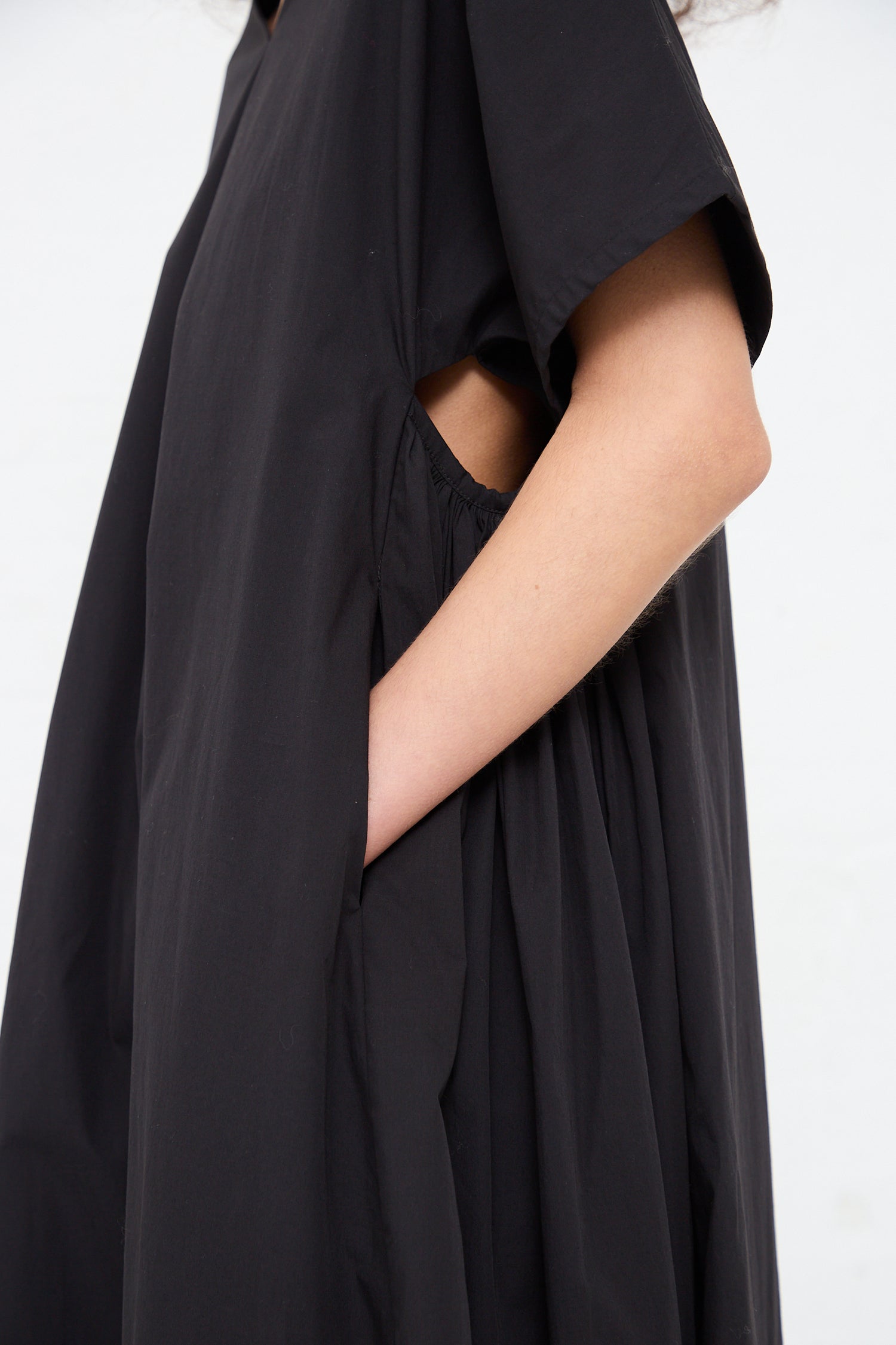 A detail of a person's arm wrapped in a draped Black Crane Organic Cotton Star Neck Dress in Black with an open sleeve, showcasing the unique elegance of Los Angeles fashion.
