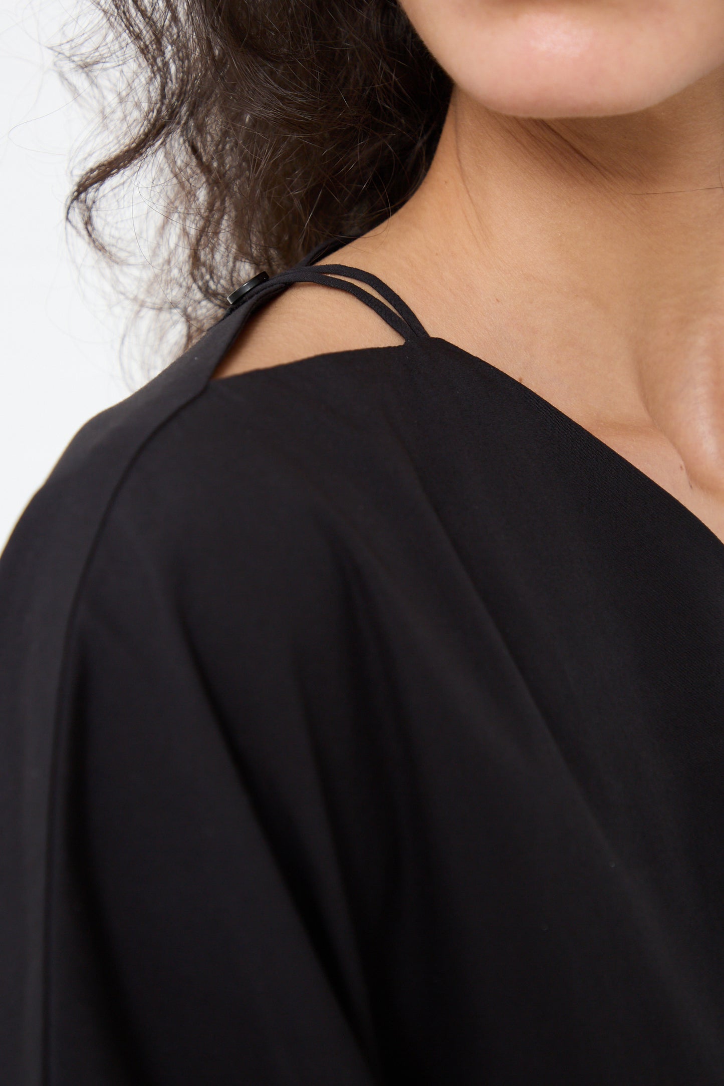 Close-up of a woman wearing a Black Crane Organic Cotton Star Neck Dress in Black with a visible strap.