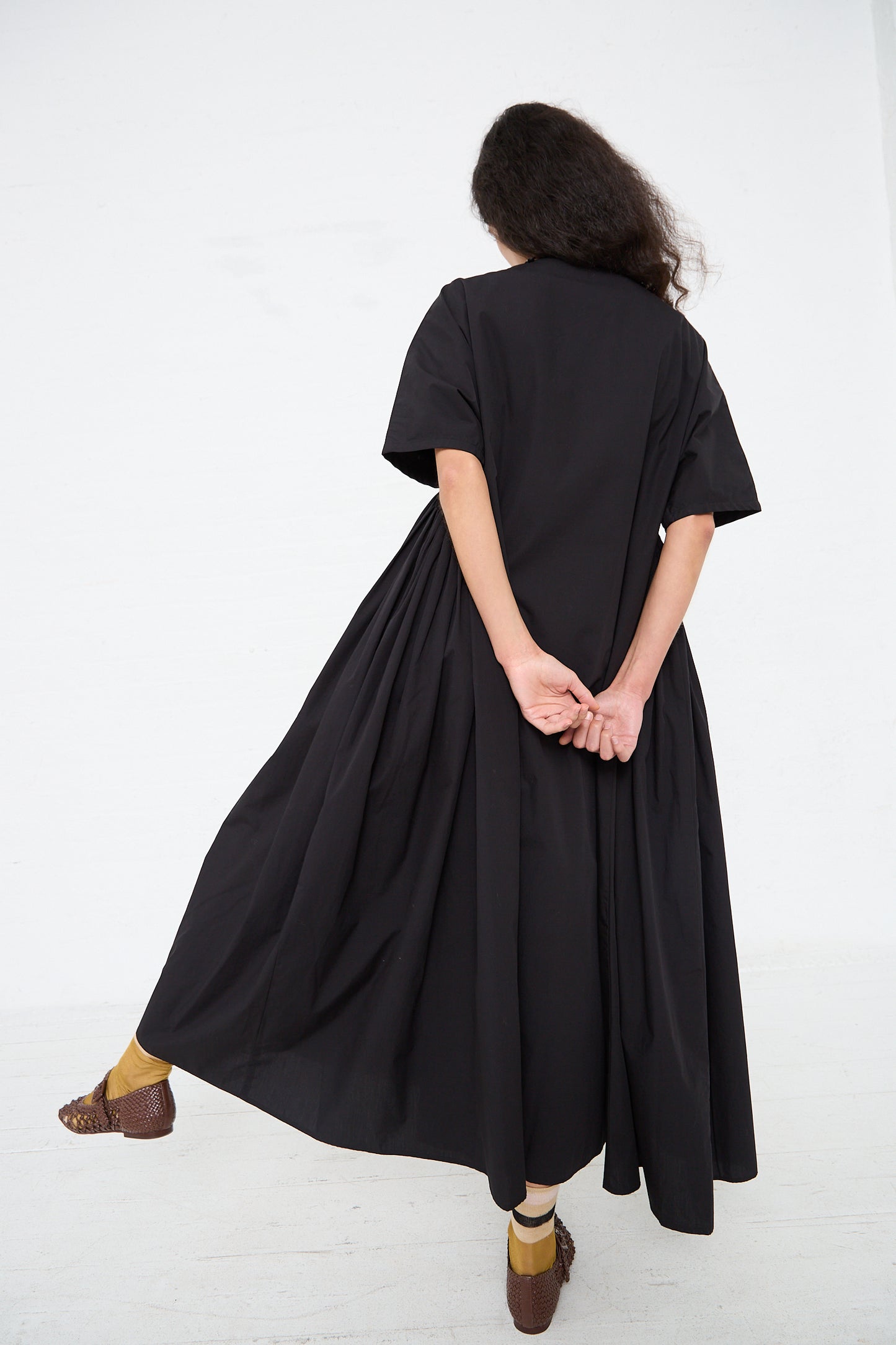 A person viewed from behind wearing a flowing Black Crane Organic Cotton Star Neck Dress in Black and patterned shoes, embodying Los Angeles fashion.