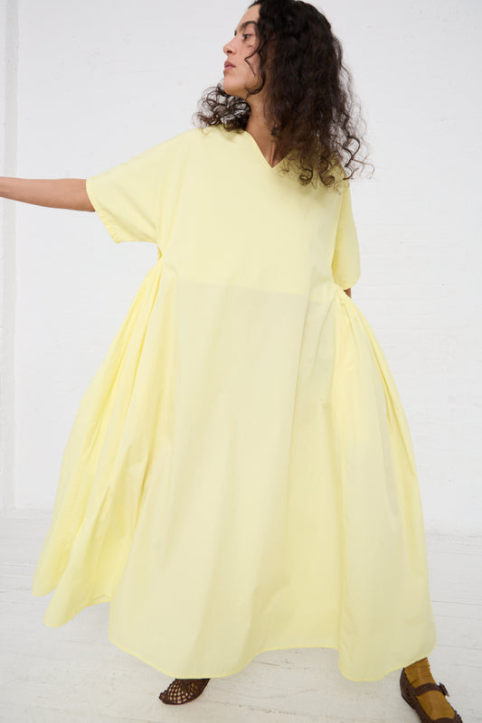 Woman in a flowing Organic Cotton Star Neck Dress in Lemon by Black Crane, with dynamic pose against a white background.