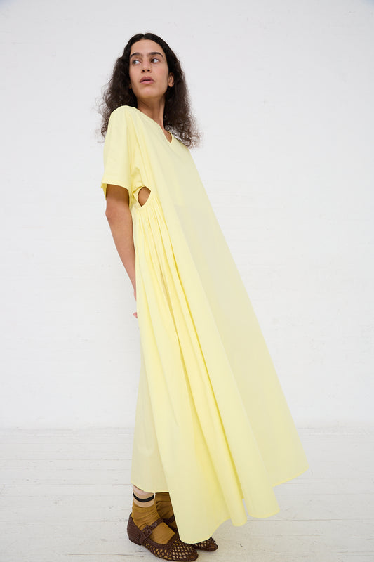 A person in Black Crane's Organic Cotton Star Neck Dress in Lemon with a unique cut-out detail stands against a white background, showcasing the Los Angeles fashion aesthetic.