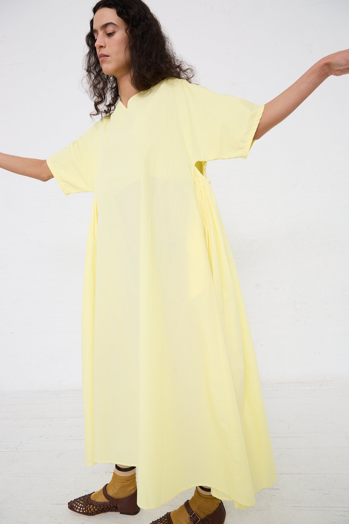 A person in a yellow oversized Black Crane Organic Cotton Star Neck Dress in Lemon with arms extended, against a white background.