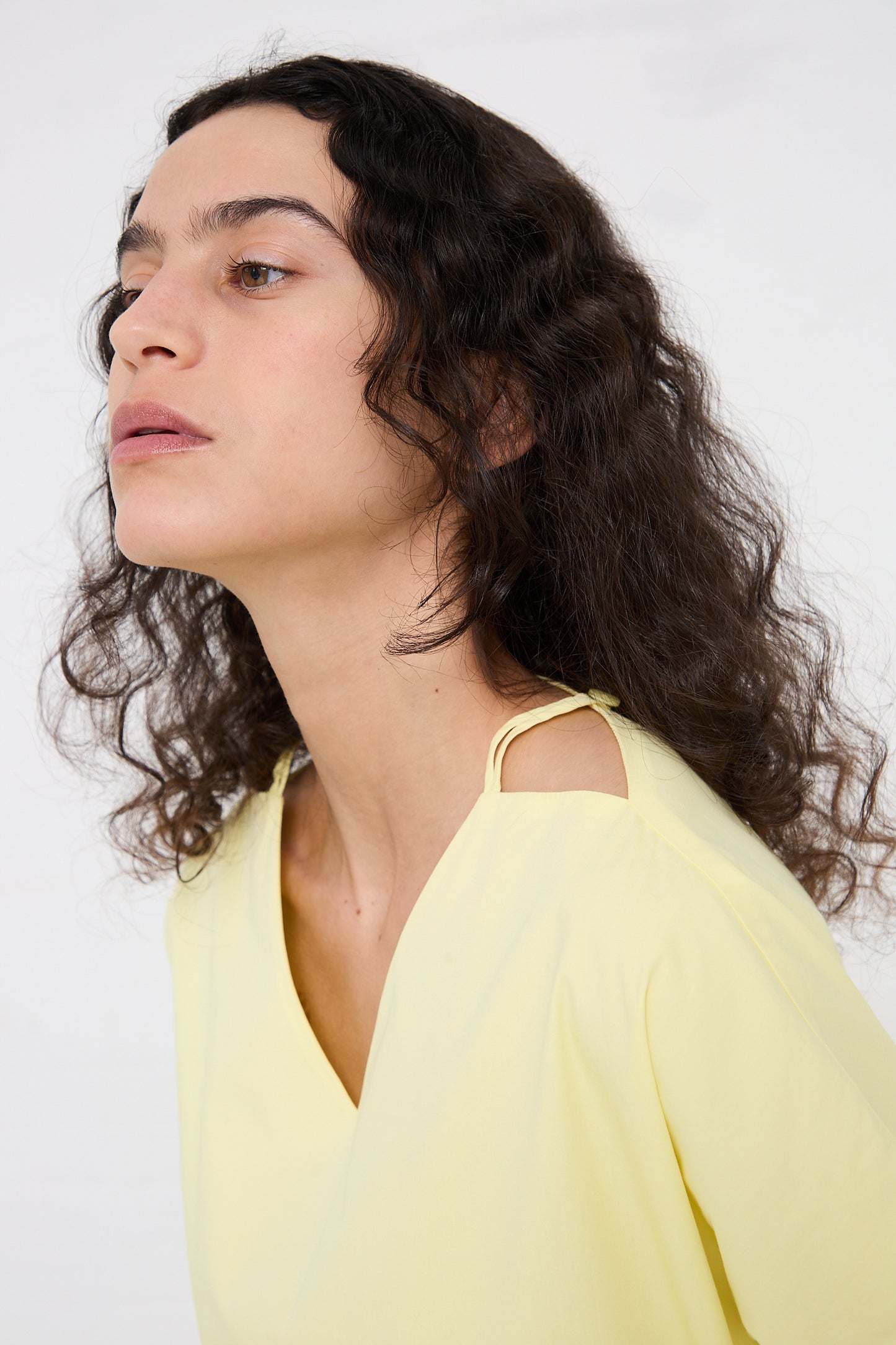 Profile view of a person with shoulder-length curly hair, wearing a Black Crane Organic Cotton Star Neck Dress in Lemon.
