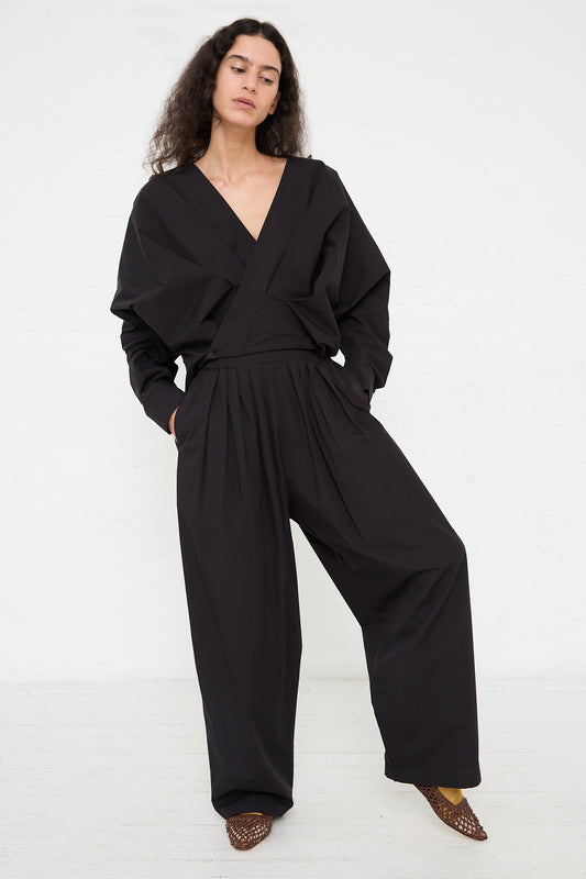 A woman poses in a Black Crane Organic Cotton Straight Draped Pant in Black and wrap-style top, complemented by pointed patterned shoes.