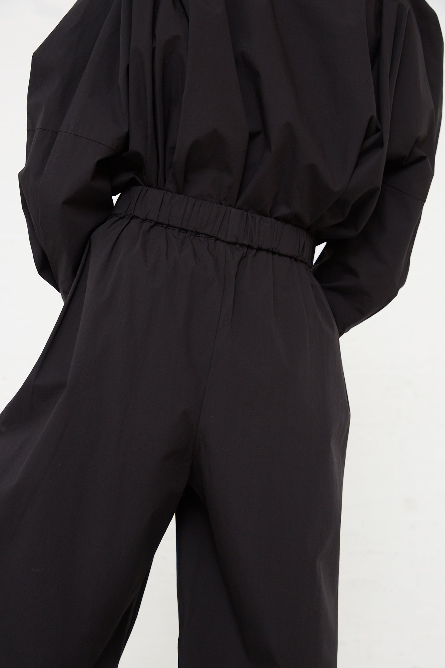 Woman wearing a Black Crane Organic Cotton Straight Draped Pant in Black, featuring a cinched waist.