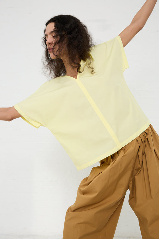 Woman in a Black Crane Organic Cotton V-Neck Top in Lemon and brown trousers, dancing or moving energetically against a white background.