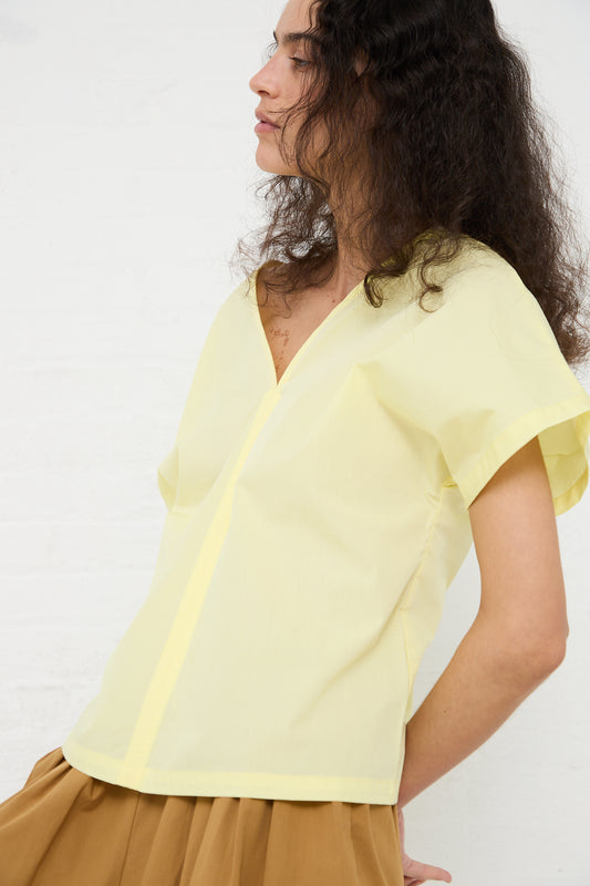 Woman wearing a Black Crane Organic Cotton V-Neck Top in Lemon with a side profile view against a white background.