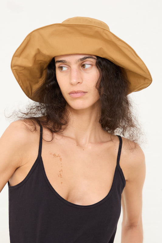 Woman wearing an oversized Black Crane Cotton Wavy Hat in Camel and Black Crane black tank top looking to the side.