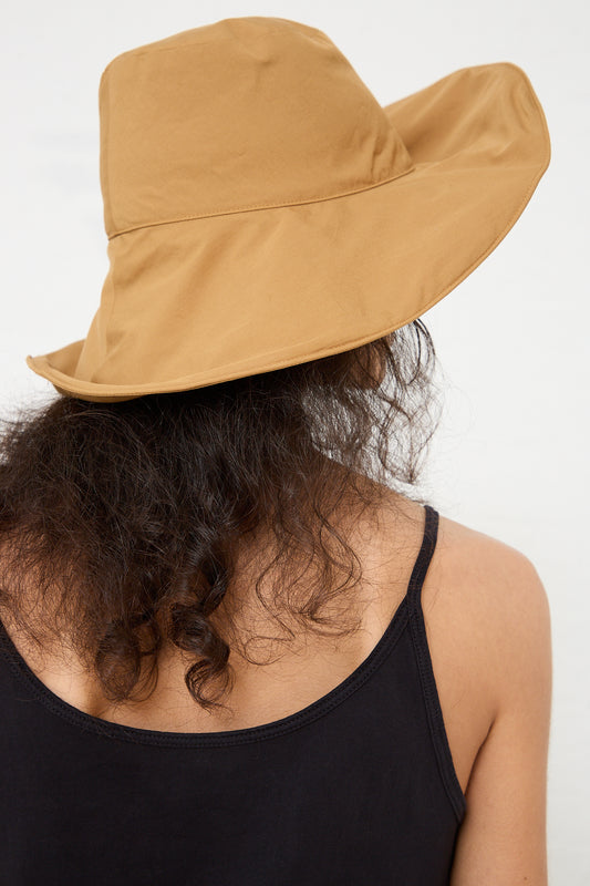 A person with curly hair wearing a wide-brimmed Black Crane Cotton Wavy Hat in Camel and a black top, photographed from the back.