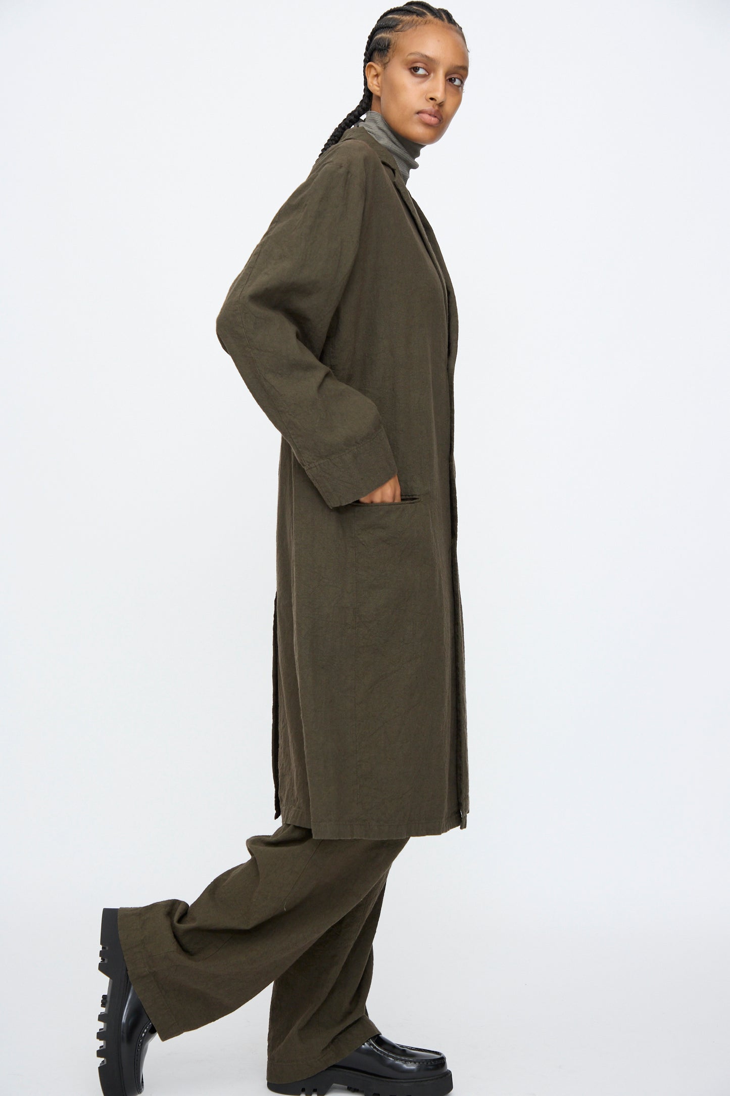 A model wears the Black Crane Crinkled Coat in Charcoal with matching pants, standing sideways with one foot slightly raised against a plain white background.