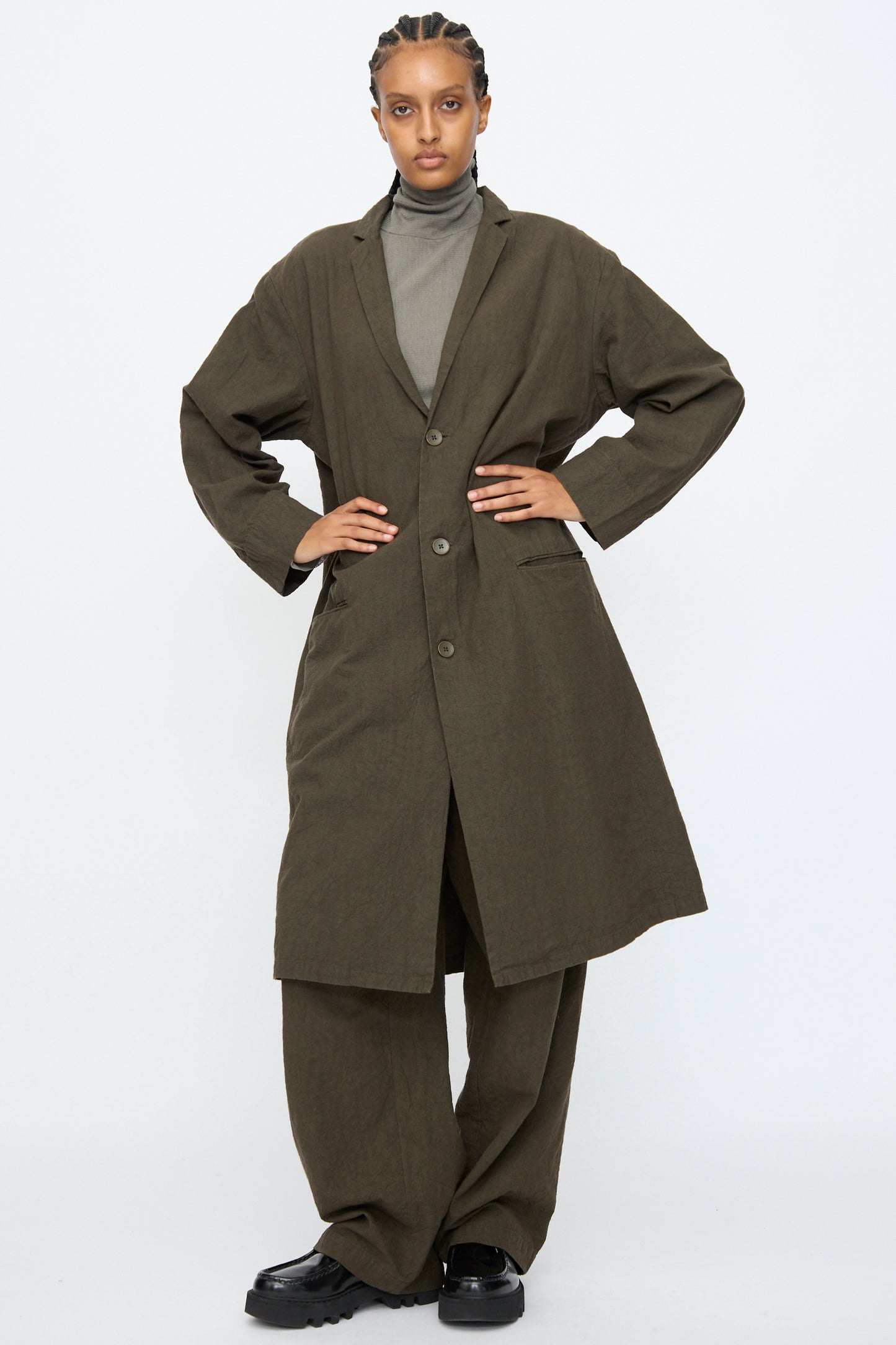 Person wearing the Black Crane Crinkled Coat in Charcoal with matching wide-leg pants, a gray turtleneck, and black shoes, standing against a plain white background.