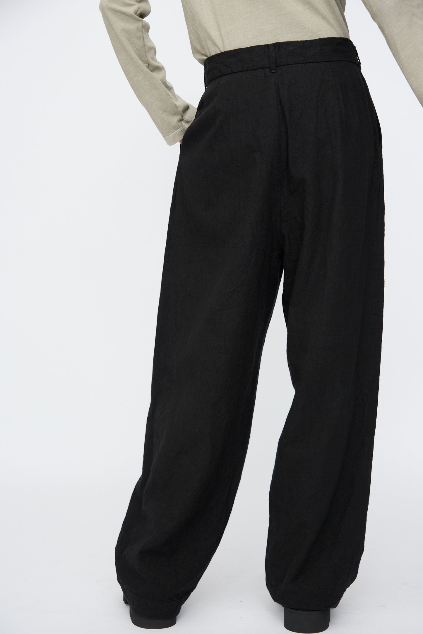 Model wears Black Crane's Crinkled Trousers in Black, styled with a beige long-sleeve top and photographed waist-down against a plain white background.