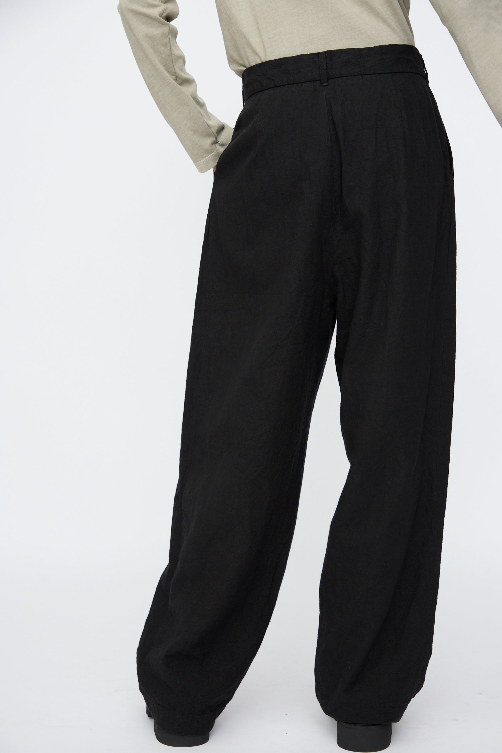Model wears Black Crane's Crinkled Trousers in Black, styled with a beige long-sleeve top and photographed waist-down against a plain white background.