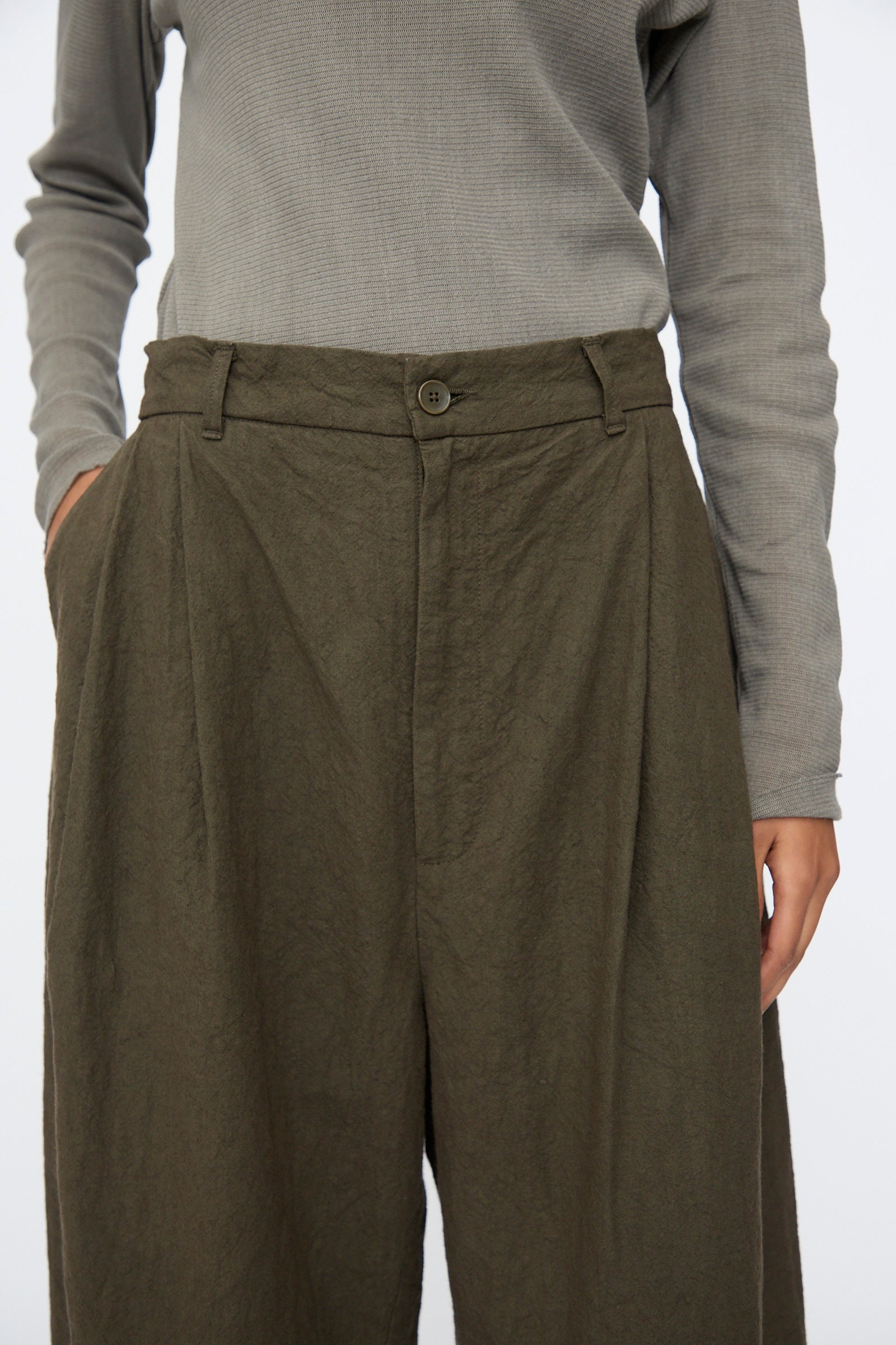 Person wearing a long-sleeve gray top and Black Crane Crinkled Trousers in Charcoal, shown from shoulders to mid-thigh.