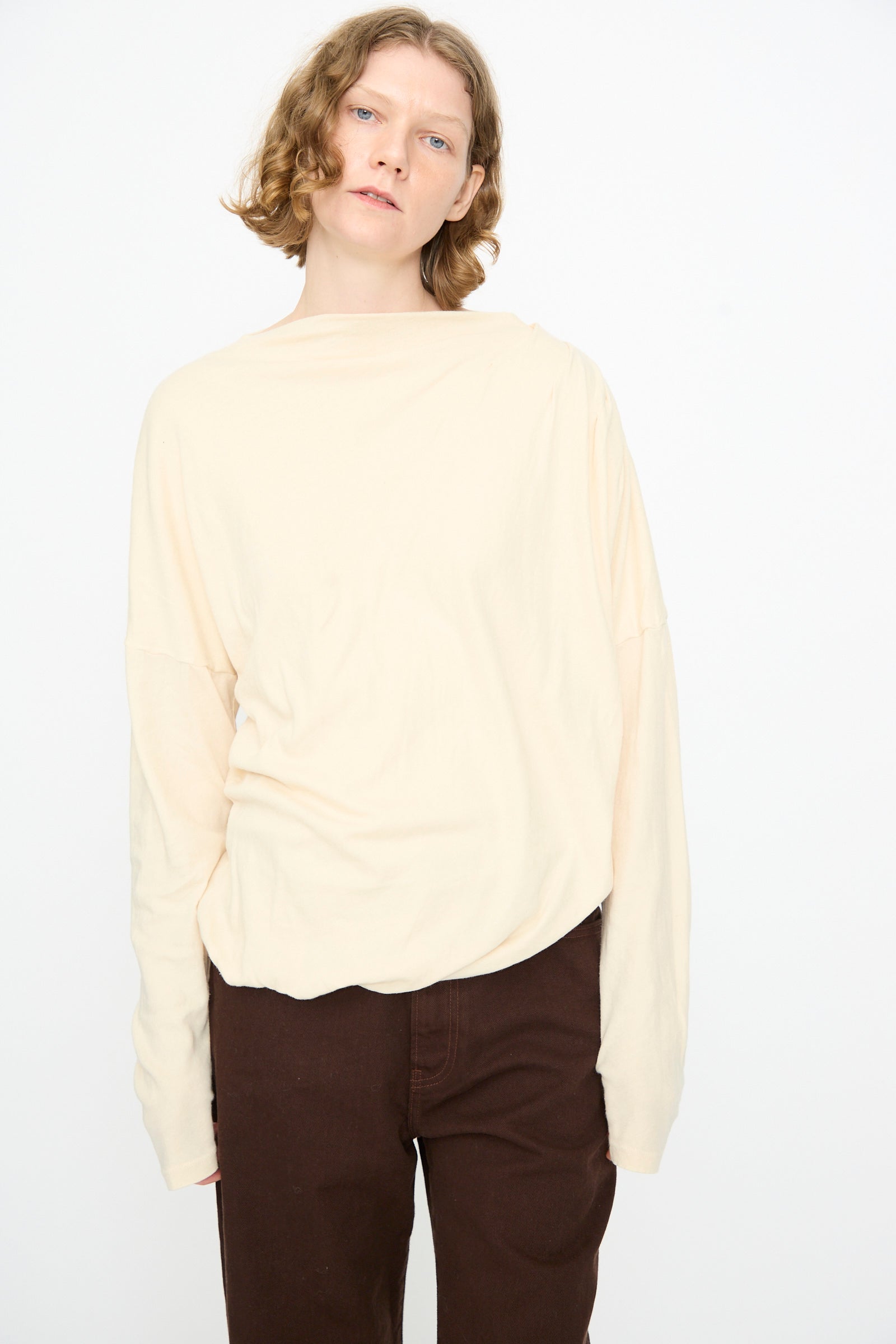 A person with short, wavy hair wears the Black Crane Double Layer Draped Top in Natural and dark brown pants, standing against a plain white background.