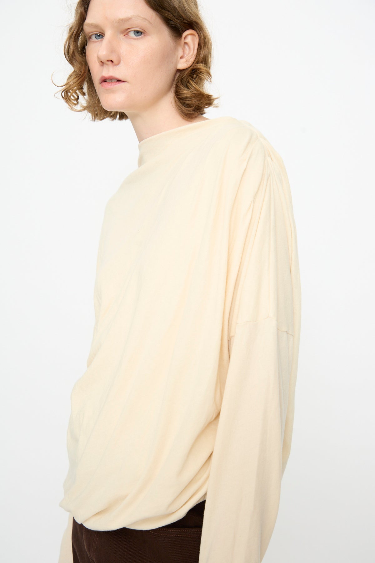A person with short, wavy hair wears the Black Crane Double Layer Draped Top in Natural and dark pants, standing against a plain white background.