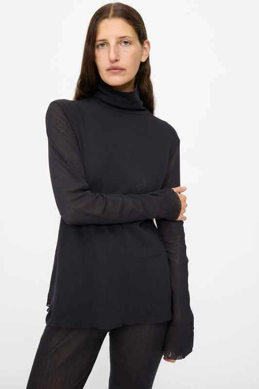 A person with long brown hair wears the Black Crane Double Mesh Turtleneck in Black and matching black pants, standing against a plain white background.