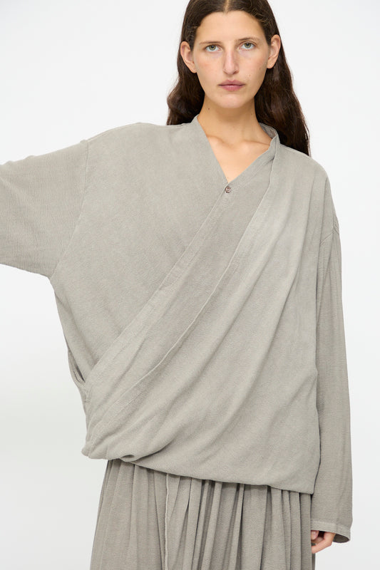 A person with long brown hair wears the Black Crane Drapy Shirt in Dark Stone, a loose-fitting cotton rayon blend top, paired with a matching skirt, standing against a plain white background.