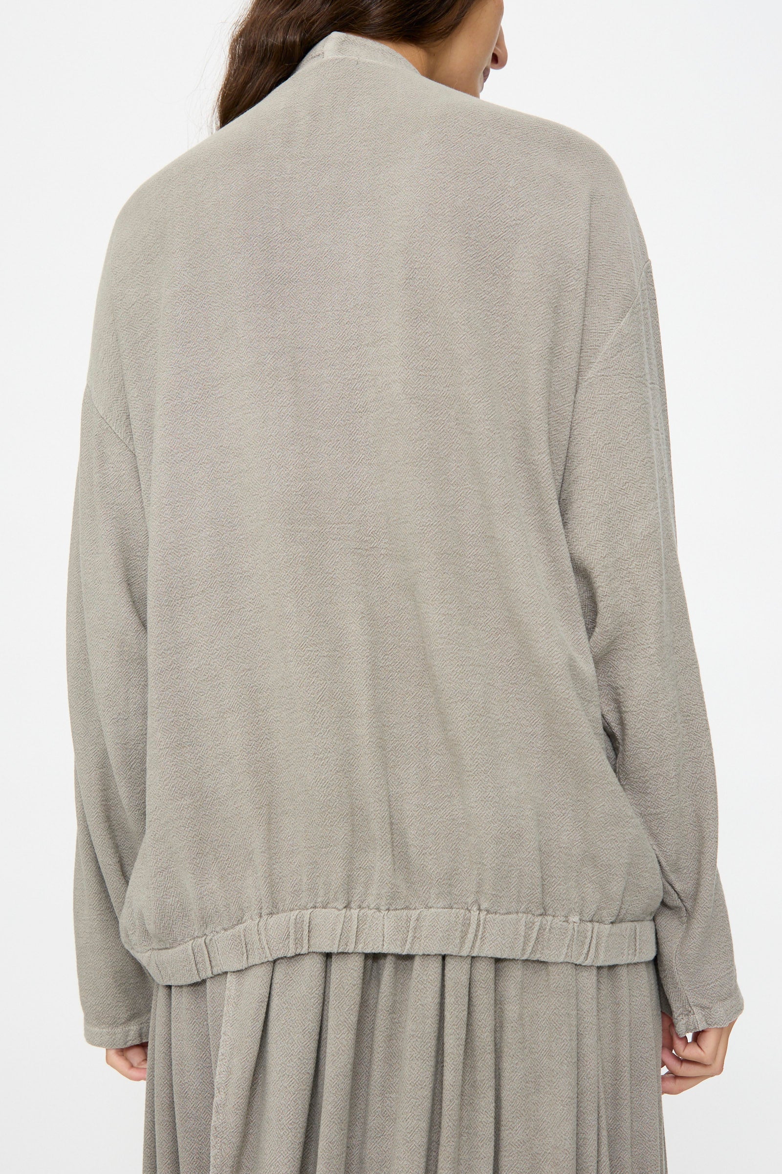 A person shown from the back wears the Black Crane Drapy Shirt in Dark Stone, paired with a matching skirt, against a plain white background.