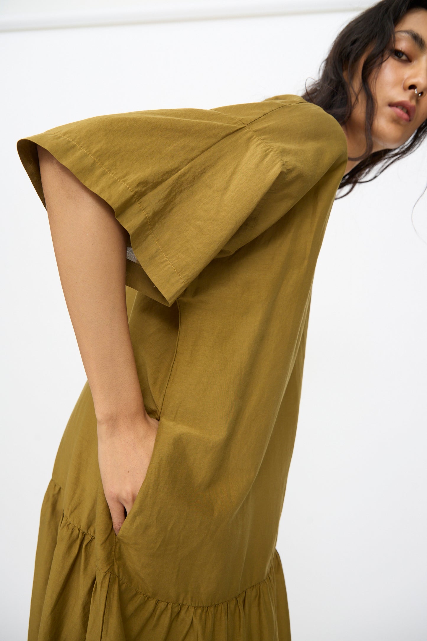 A person models the Black Crane Easy Dress in Dark Olive—an oversized, short-sleeve maxi dress in a cotton silk blend—standing slightly sideways against a plain white background.
