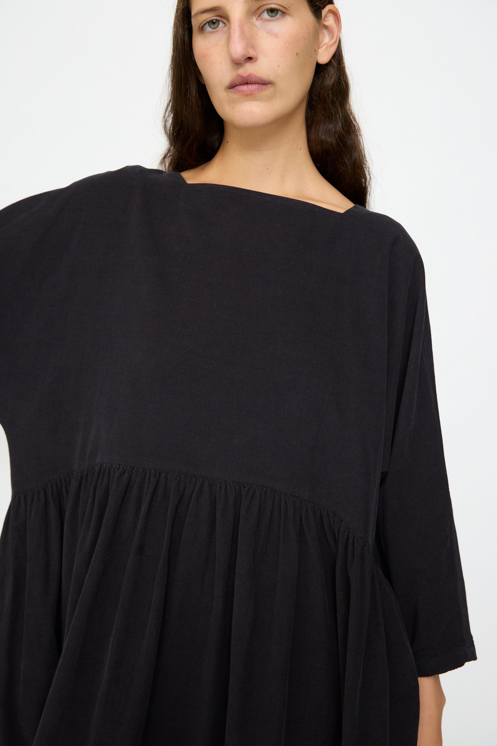 A person with long brown hair wears the Black Crane Tradi Dress in Dark Navy—an oversized fit with a wide neckline and gathered waist—standing against a plain white background.