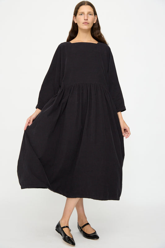 A woman stands against a white background, wearing the Black Crane Tradi Dress in Dark Navy with black flat shoes.