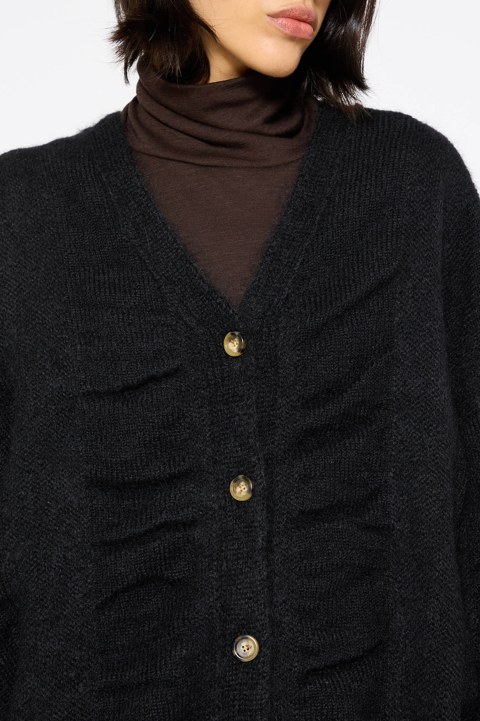 Close-up of a person wearing a dark brown turtleneck and an oversized Black Crane Japanese Mohair and Wool Waterfall Cardigan in Black with four buttons. The face is partially visible, and the background is plain white.