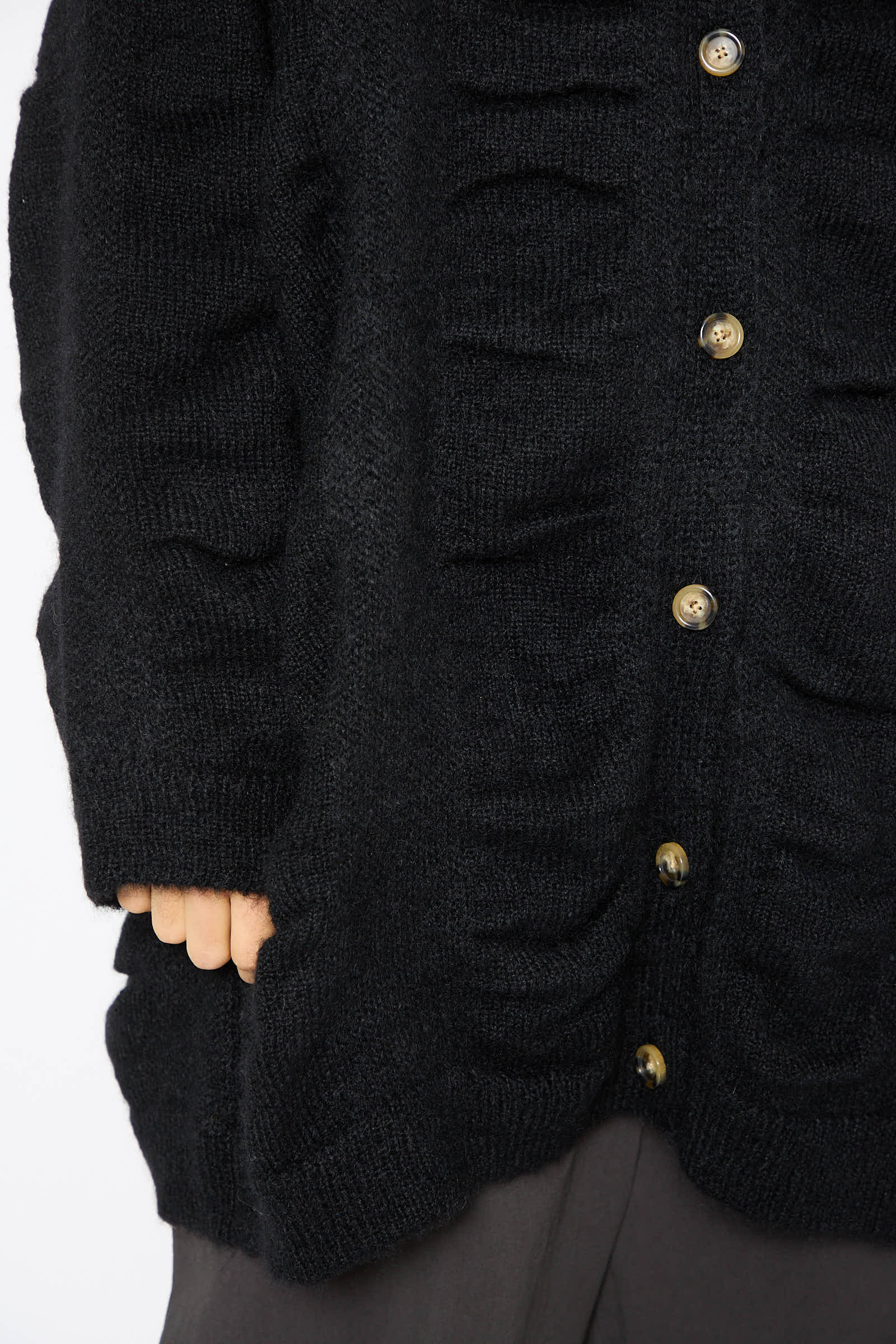 Close-up of a person wearing the Japanese Mohair and Wool Waterfall Cardigan in Black by Black Crane. The oversized, black textured knit cardigan with button details, featuring a subtle waterfall knit design and ruched elements, is paired elegantly with dark pants.