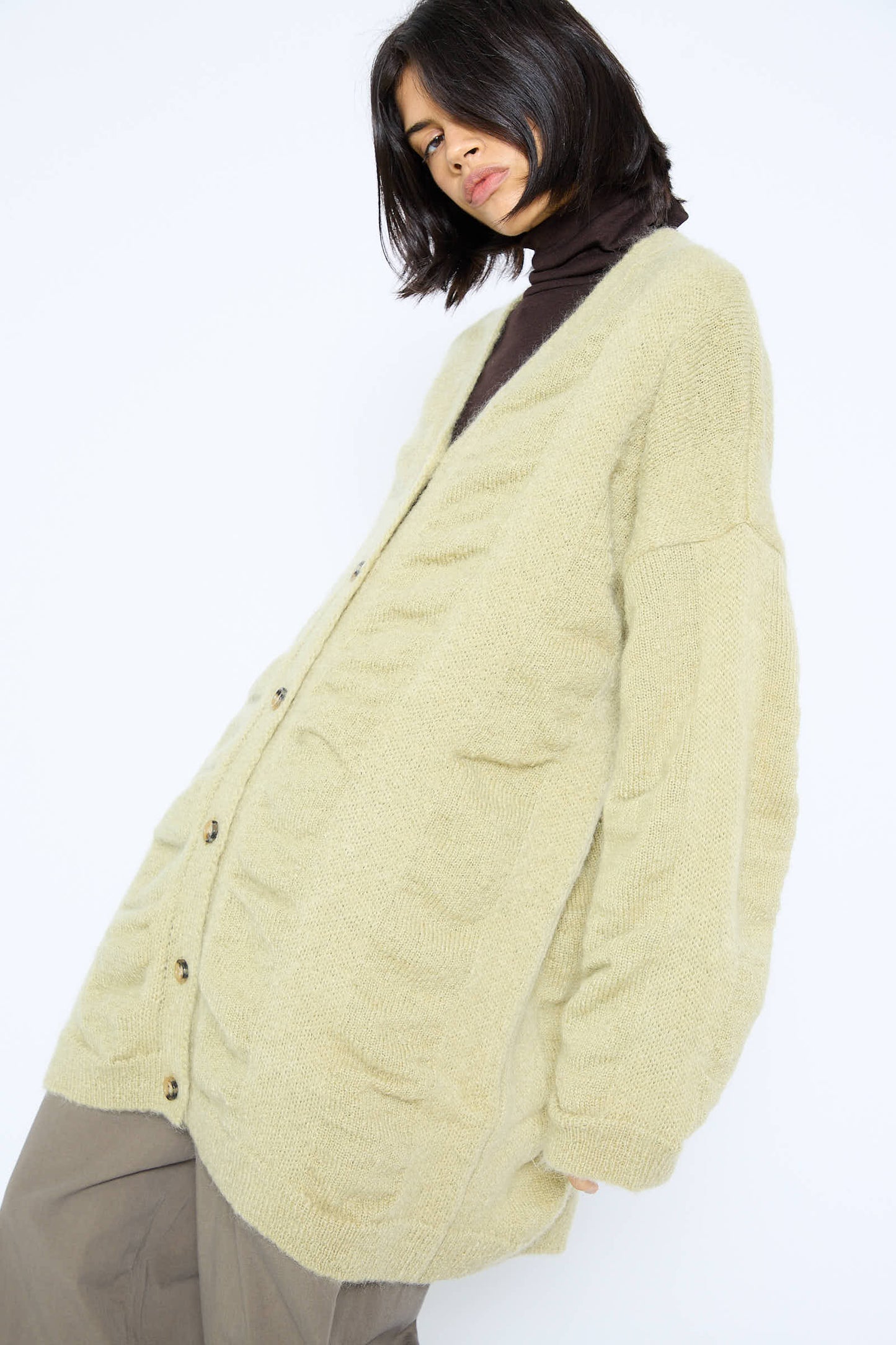 Person wearing a Japanese Mohair and Wool Waterfall Long Cardigan in Lime by Black Crane over a brown turtleneck and pants, tilting their body slightly.