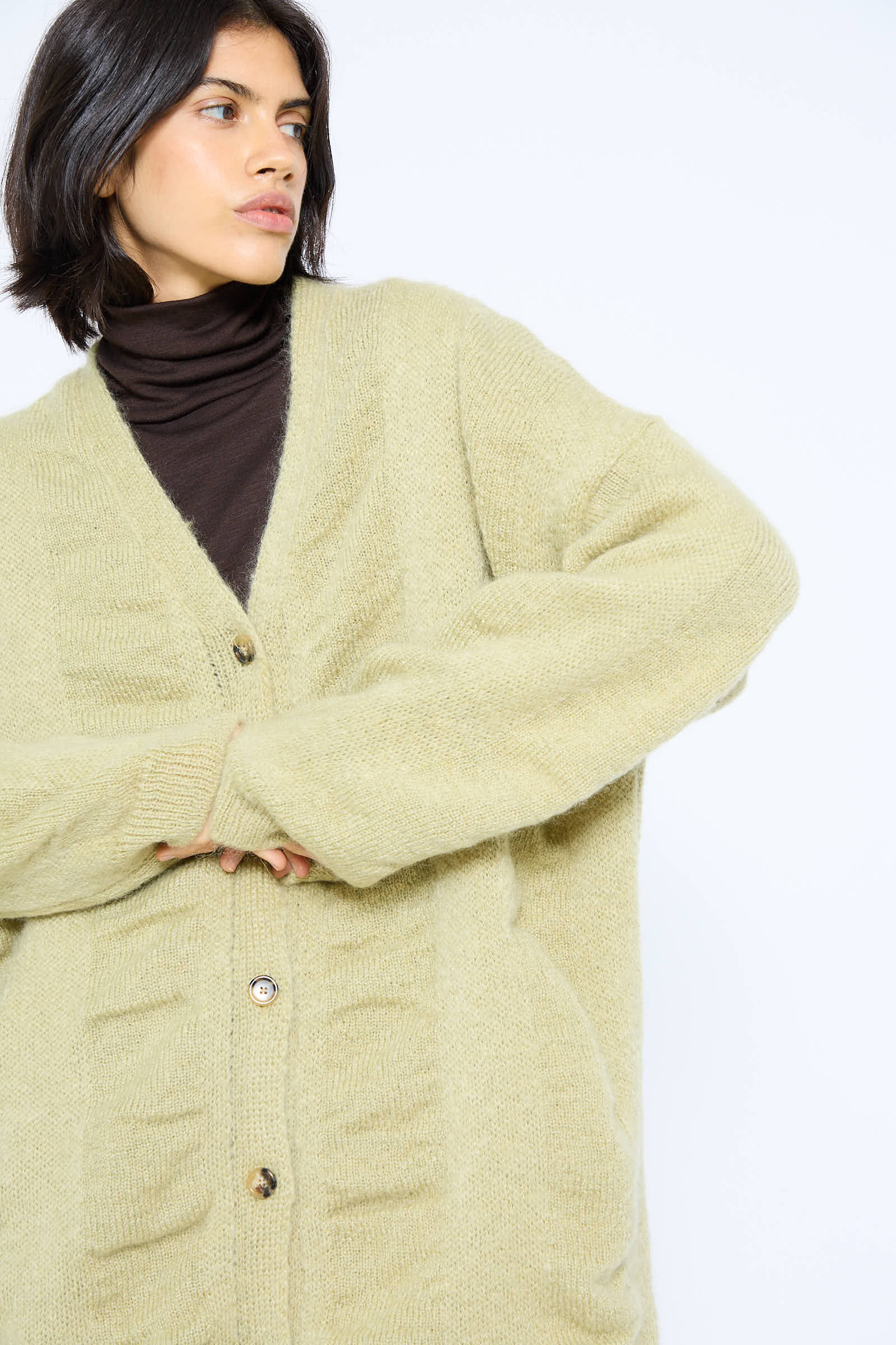 A person with short, dark hair is wearing the Black Crane Japanese Mohair and Wool Waterfall Long Cardigan in Lime over a dark turtleneck. They are looking to the left against a plain background.