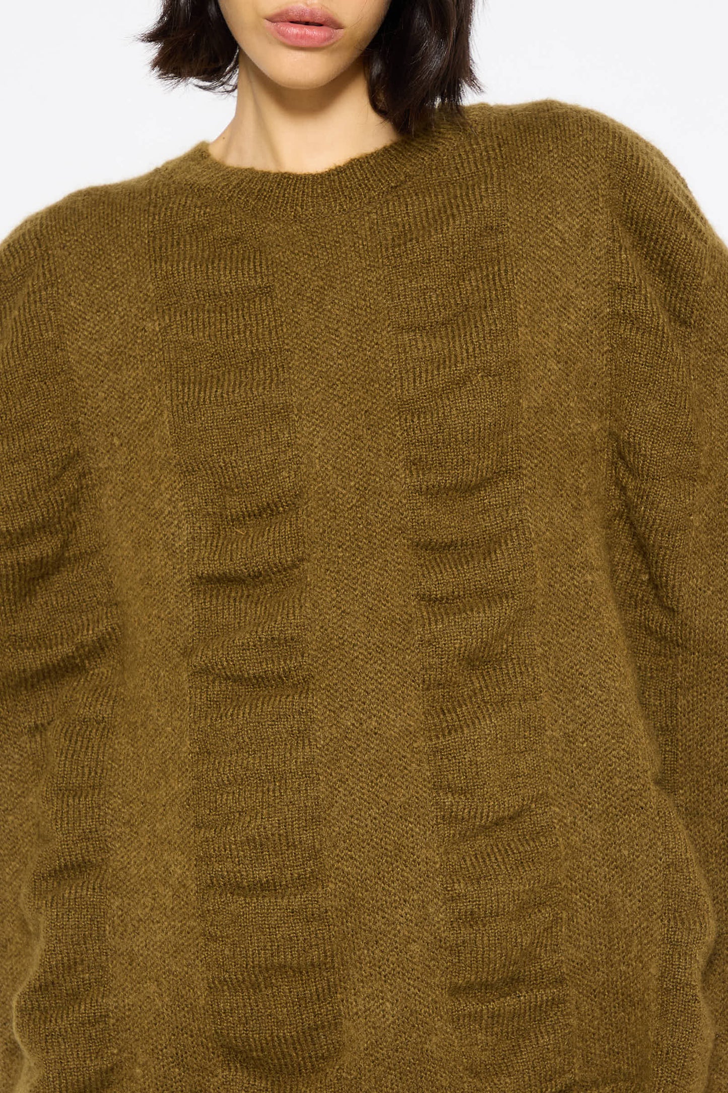 Close-up of a person wearing a Black Crane oversized Japanese Mohair and Wool Waterfall Sweater in Dark Olive. The individual's head is partially visible, with hair falling to the side.