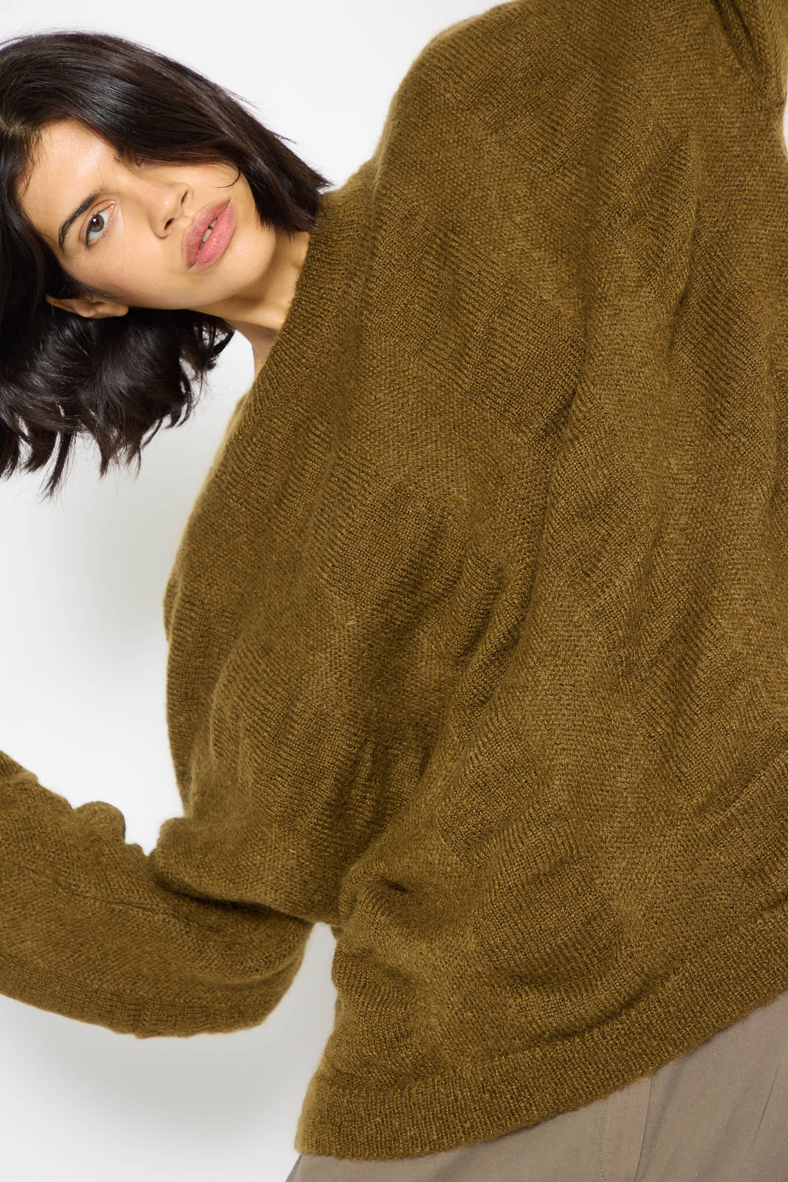 A person with shoulder-length dark hair wearing an oversized, Dark Olive Japanese Mohair and Wool Waterfall Sweater by Black Crane.