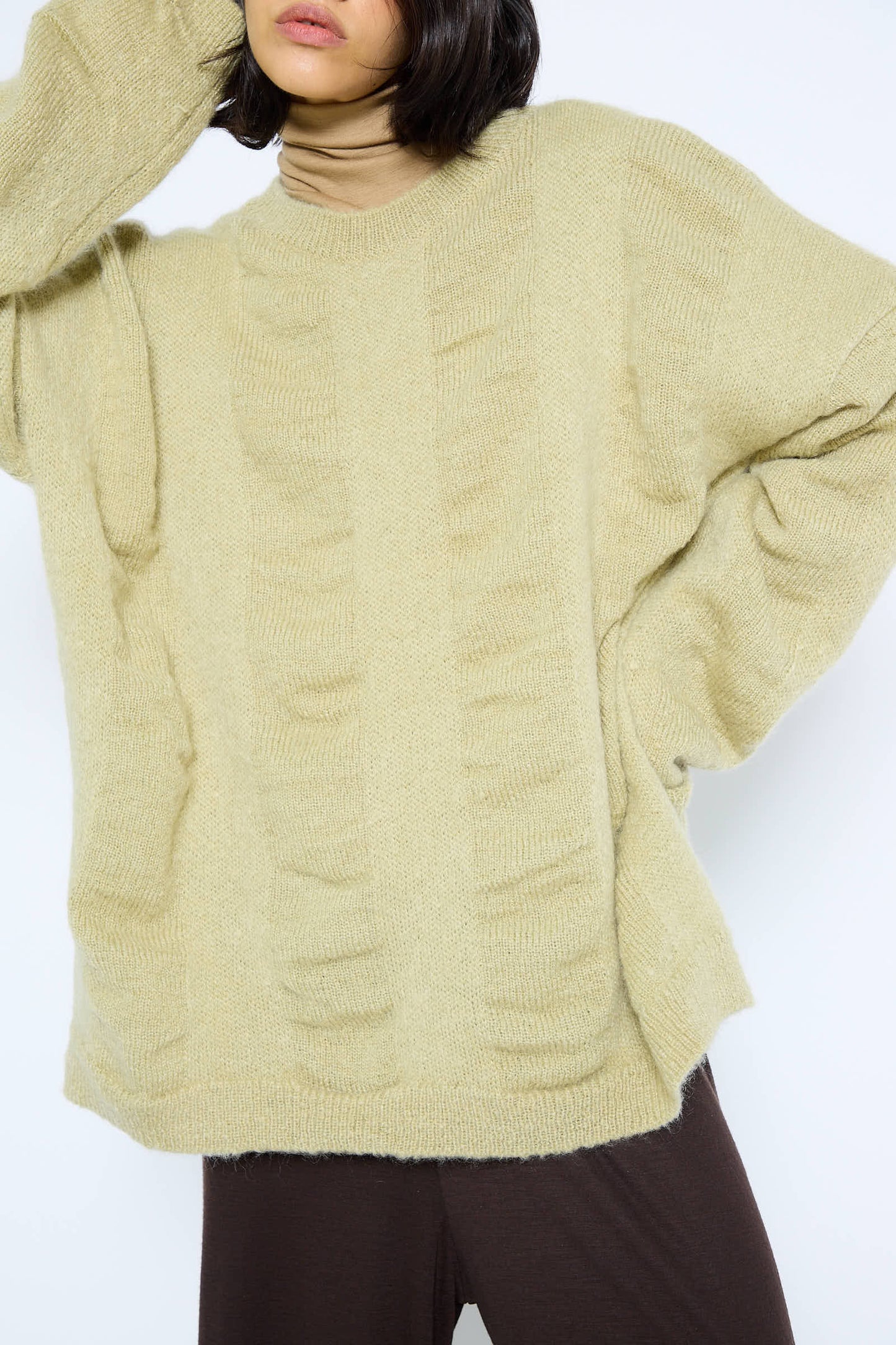 Person wearing an oversized lime Japanese Mohair and Wool Waterfall Sweater by Black Crane and brown pants against a plain white background.