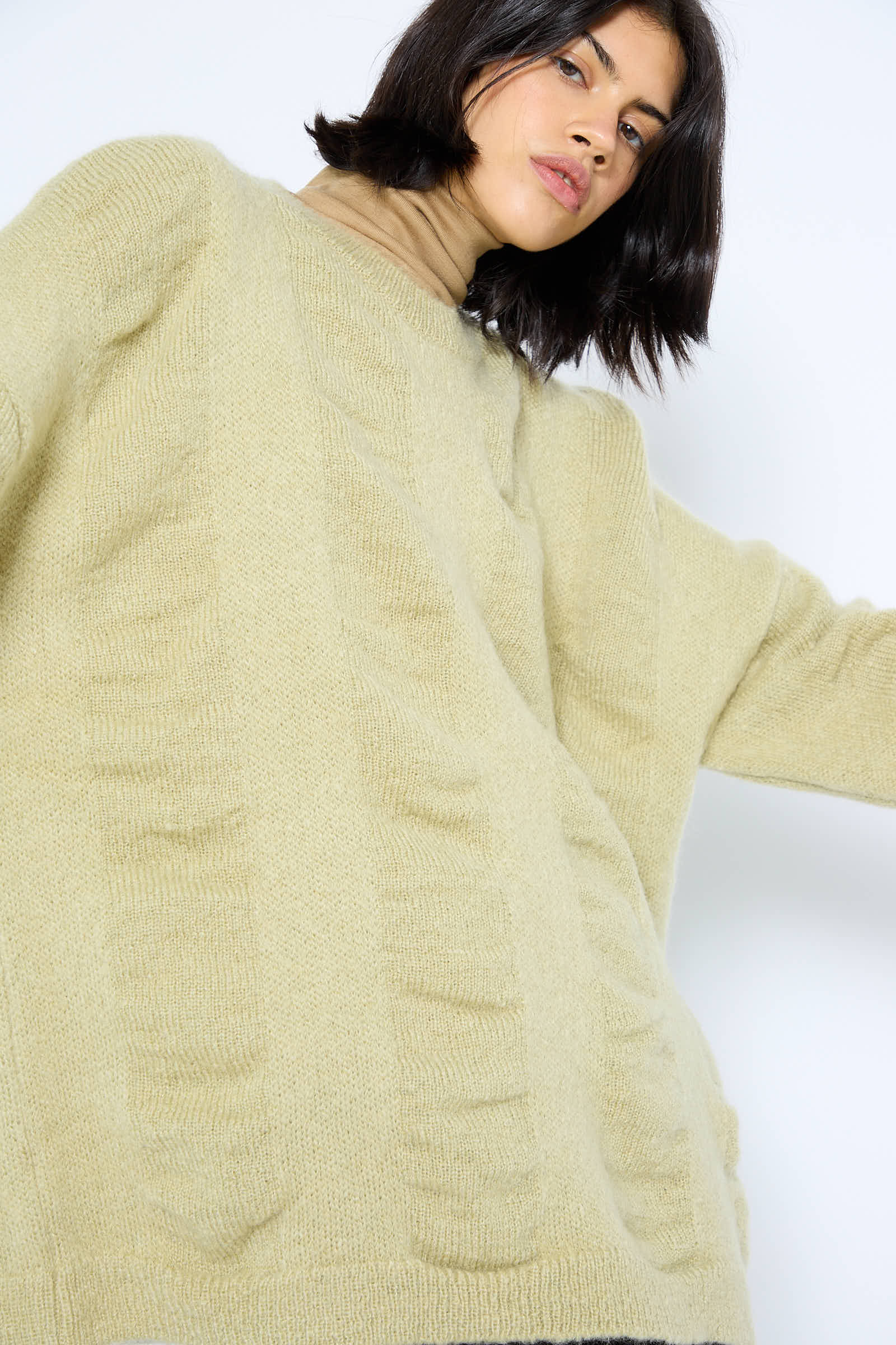 A person wearing the Black Crane Japanese Mohair and Wool Waterfall Sweater in Lime over a turtleneck looks slightly downward.