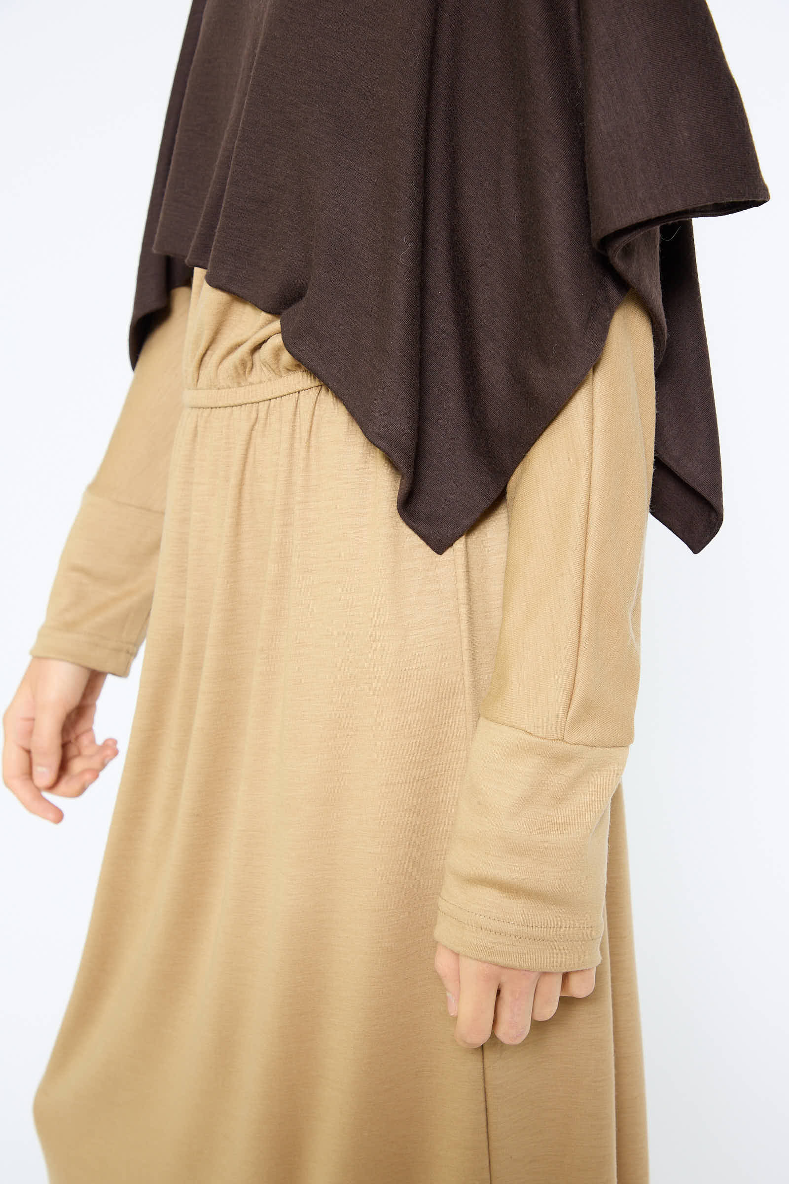 Person wearing a beige long-sleeve dress with a dark brown headscarf draped over the shoulders, accentuated by Black Crane's Japanese Wool Jersey Mini Poncho in Cacao that adds an extra layer of elegance.