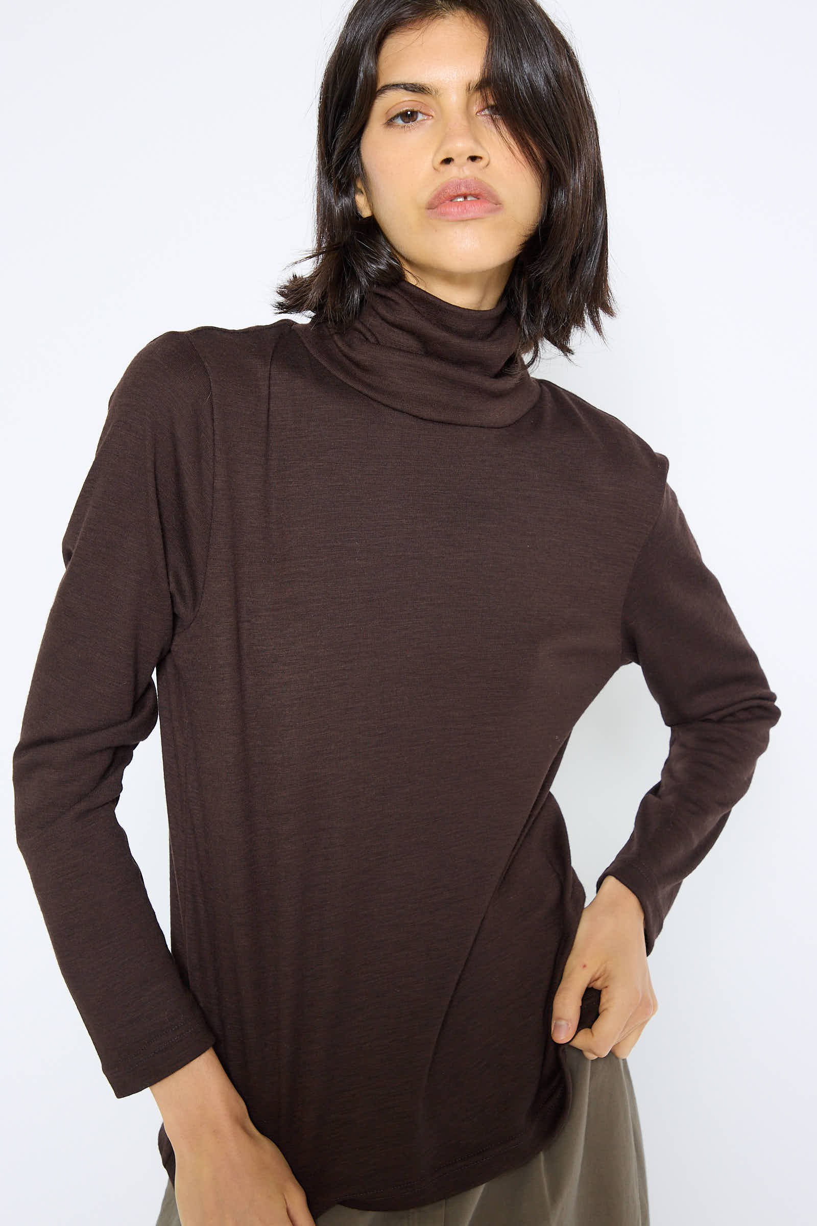 A person wearing the Black Crane Japanese Wool Jersey Turtleneck in Cacao stands against a plain white background.