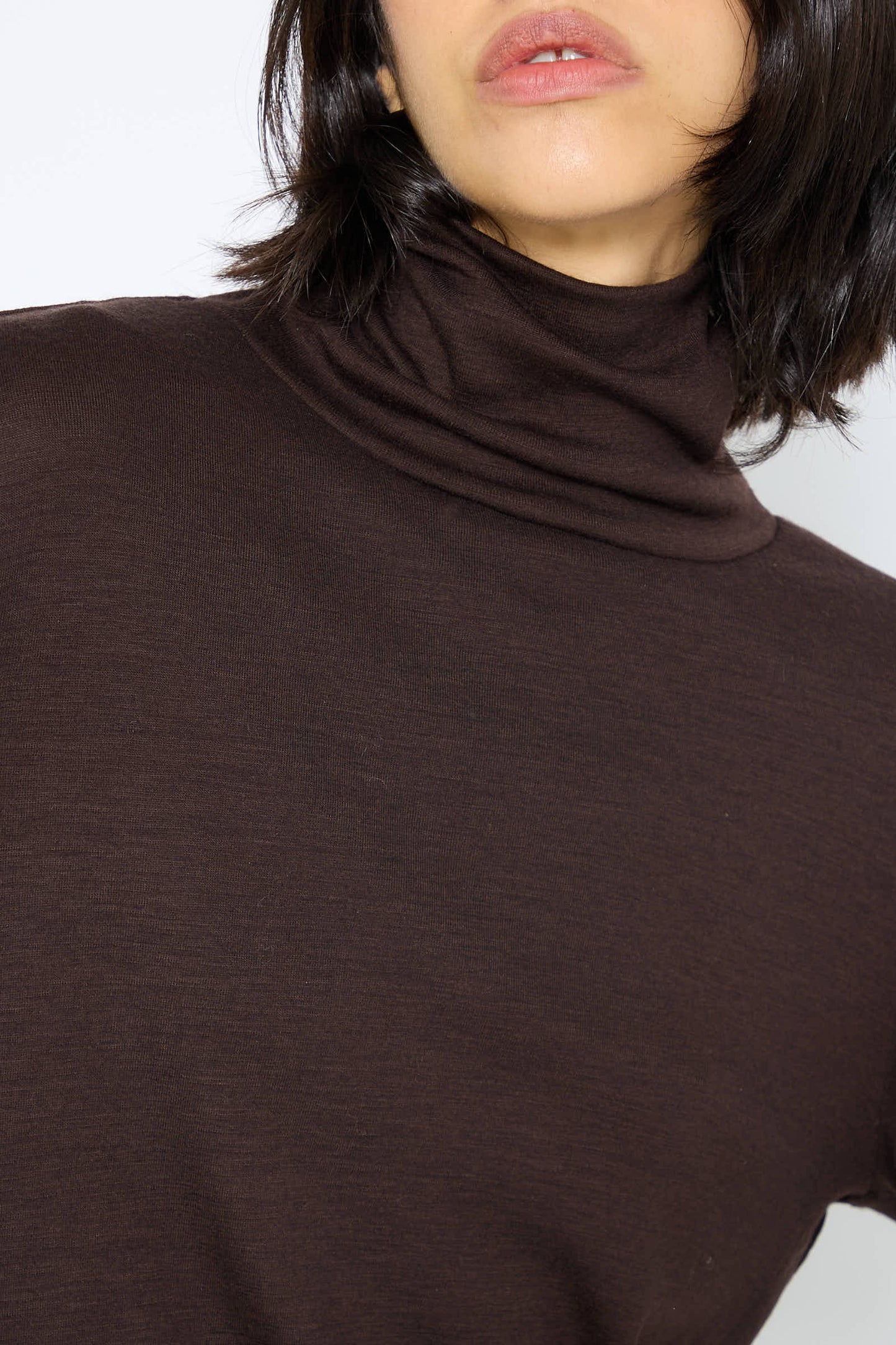 Close-up of a person wearing the Japanese Wool Jersey Turtleneck in Cacao by Black Crane. Their face is partially visible.