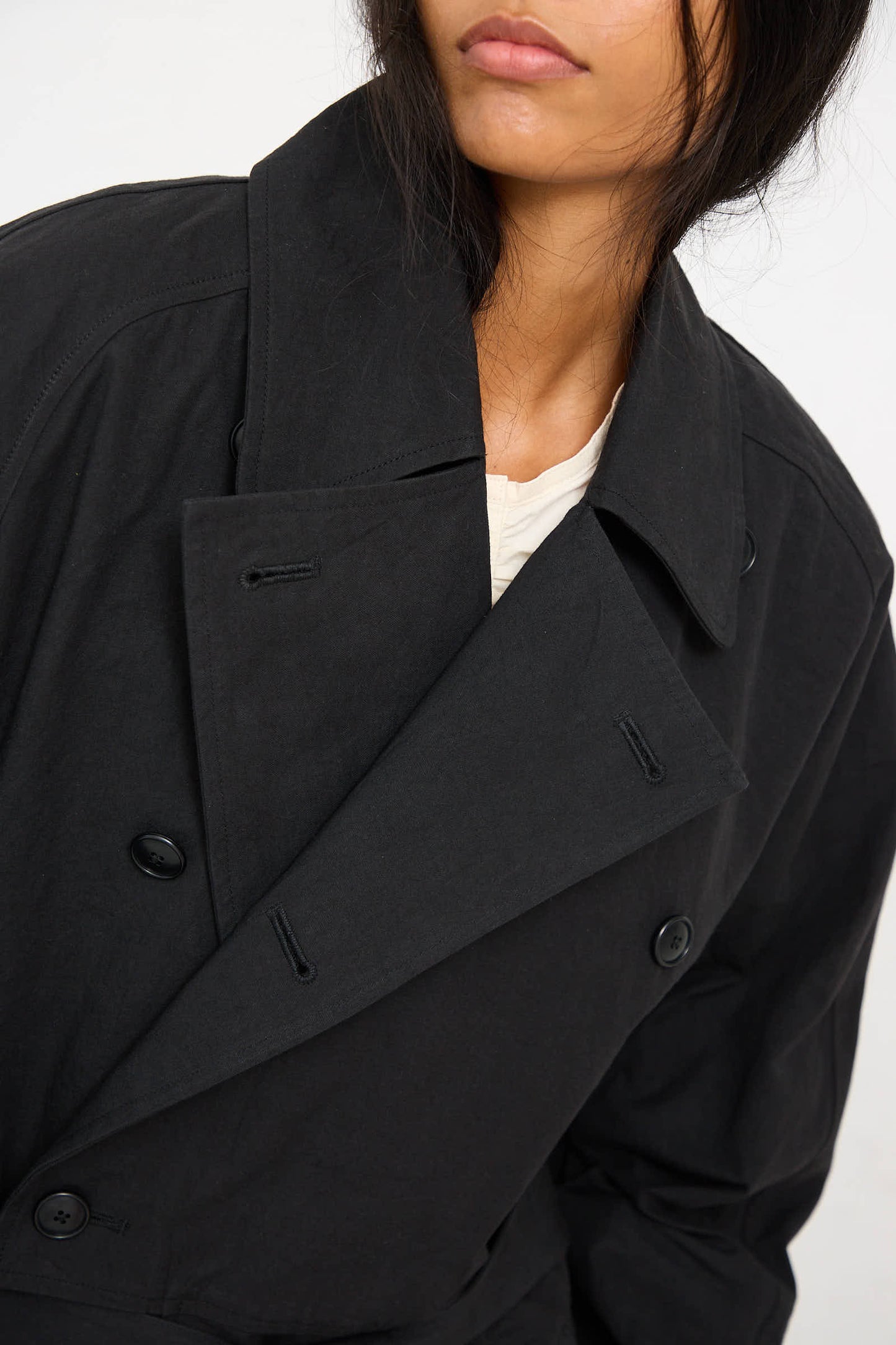 A person wearing a Woven Cotton Long Coat in Black by Black Crane over a white shirt.