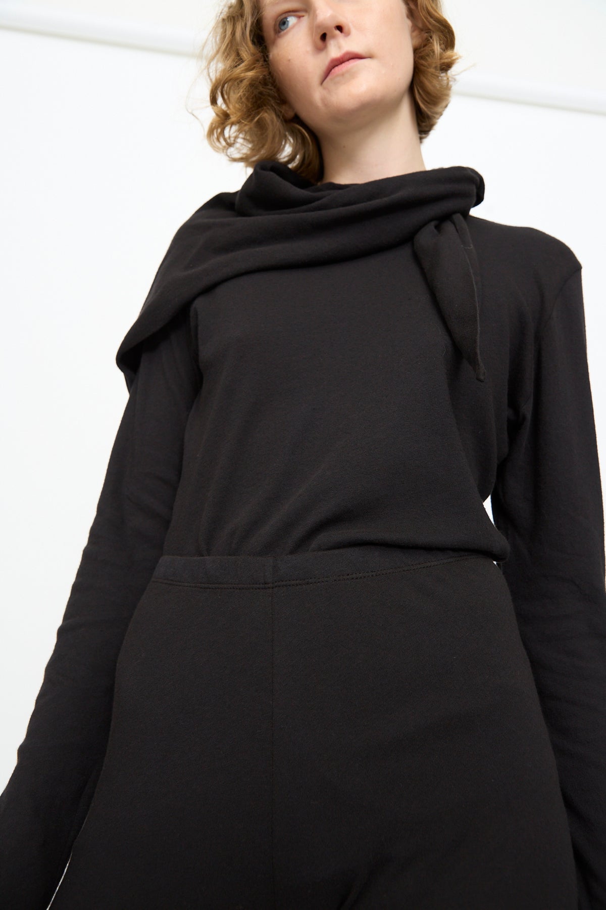 A person wearing the Black Crane Leggings in Black paired with a black long-sleeve top and a matching black scarf, standing against a plain white background.