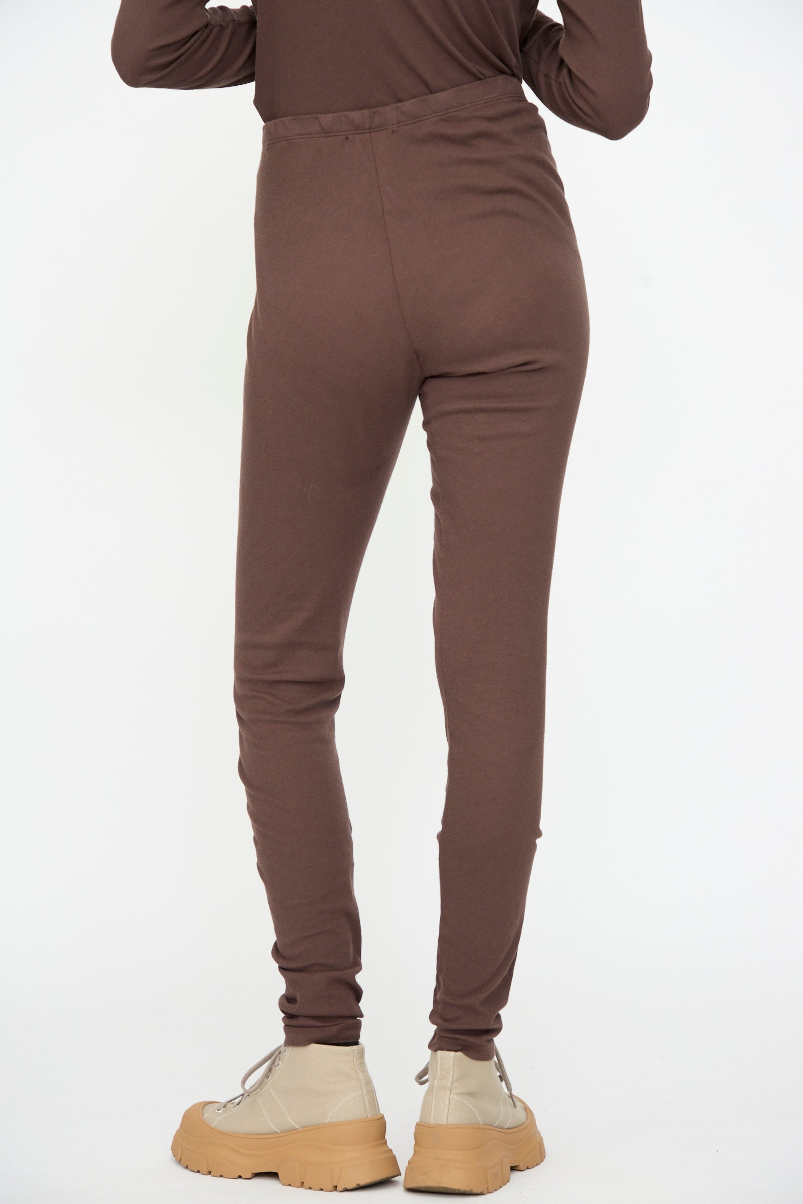 Person wearing Black Crane Leggings in Dark Plum and beige lace-up shoes, standing with their back facing the camera against a plain white background.