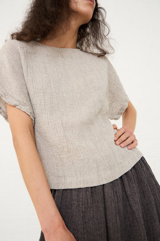 Woman wearing a textured Linen Basic Crew Top in Ash by Black Crane and a pleated dark skirt, made in Los Angeles.