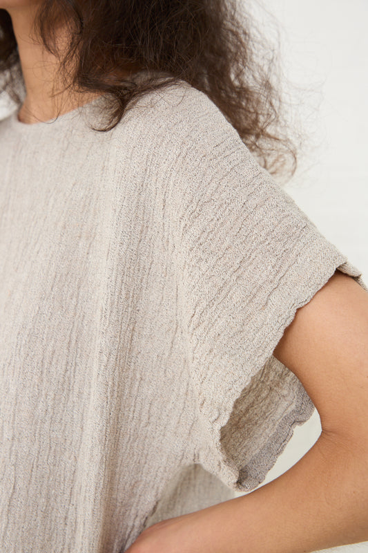 A close-up of a person wearing a Linen Basic Crew Top in Ash from Black Crane with a torn sleeve in a relaxed fit.