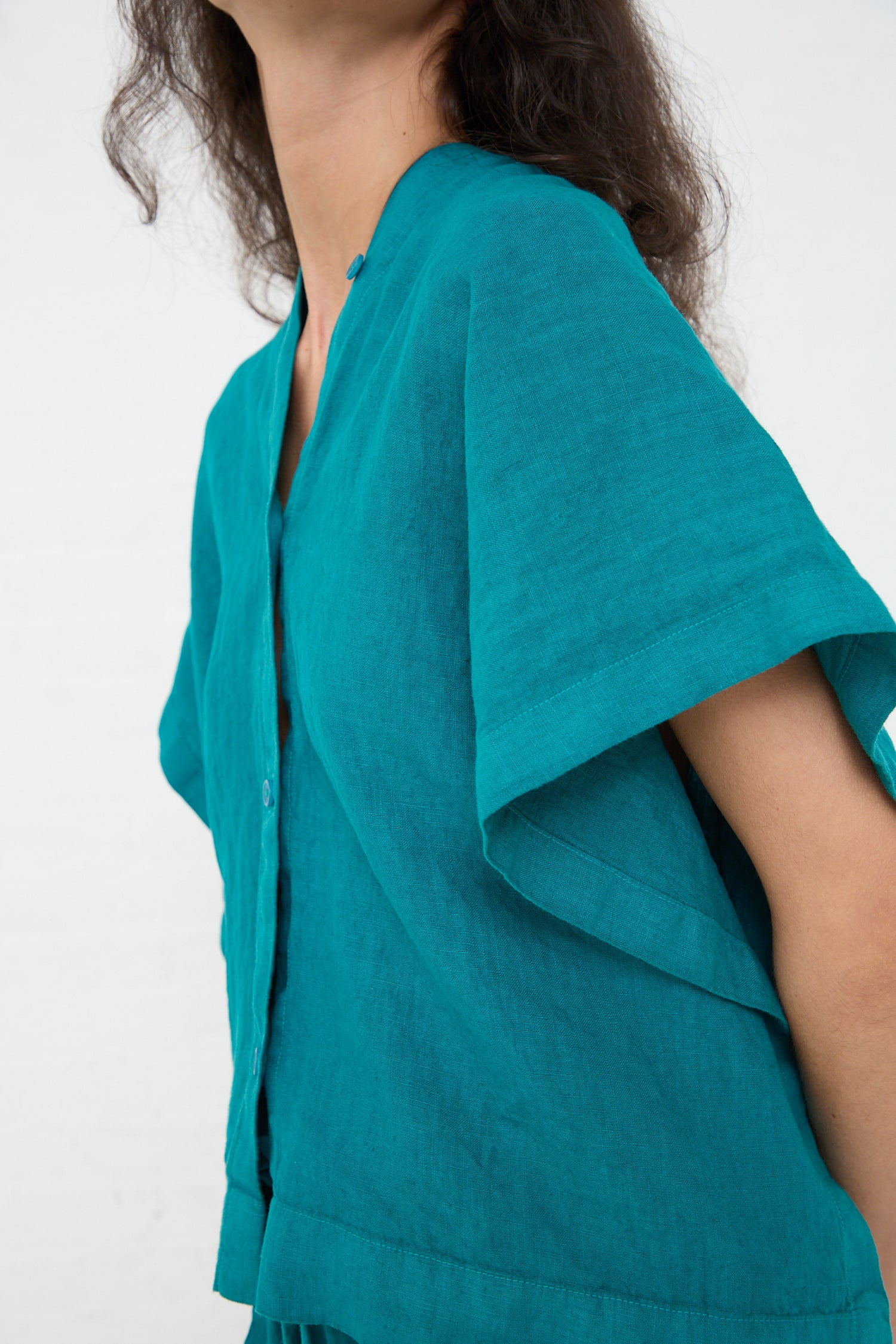 A person wearing a Linen Origami Top in Peacock by Black Crane, photographed from the side with a focus on the shoulder area against a white background.
