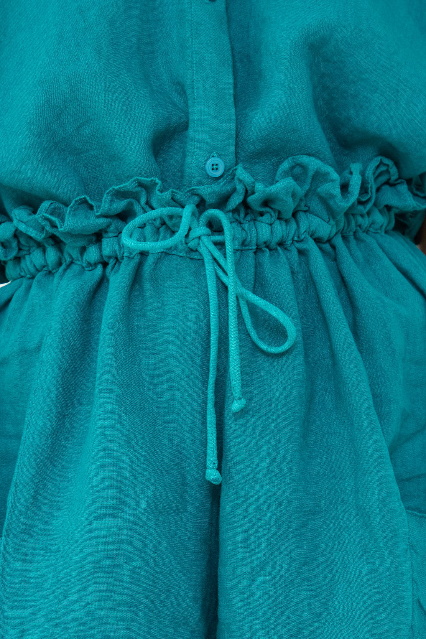 Close-up of a Peacock Linen Parachute Short by Black Crane with a buttoned front and gathered waist tied with a drawstring.